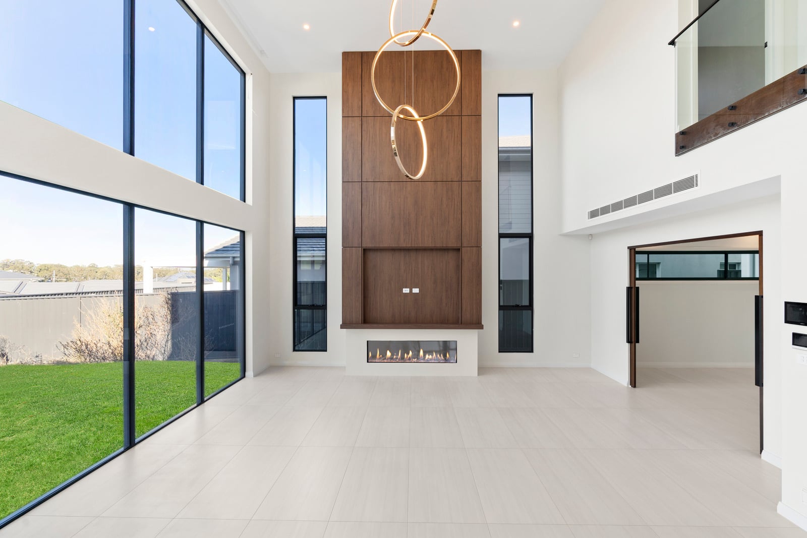 Double-height living room at Oran Park with Escea DS1650 gas fireplace burning in timber feature wall