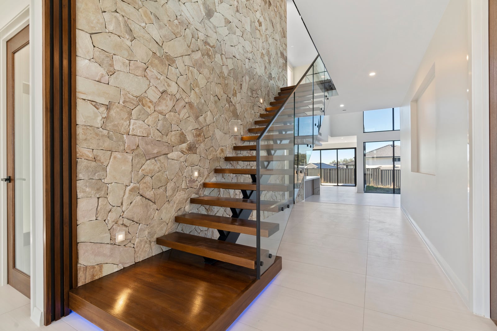 Floating timber staircase against stone feature wall, Oran Park project
