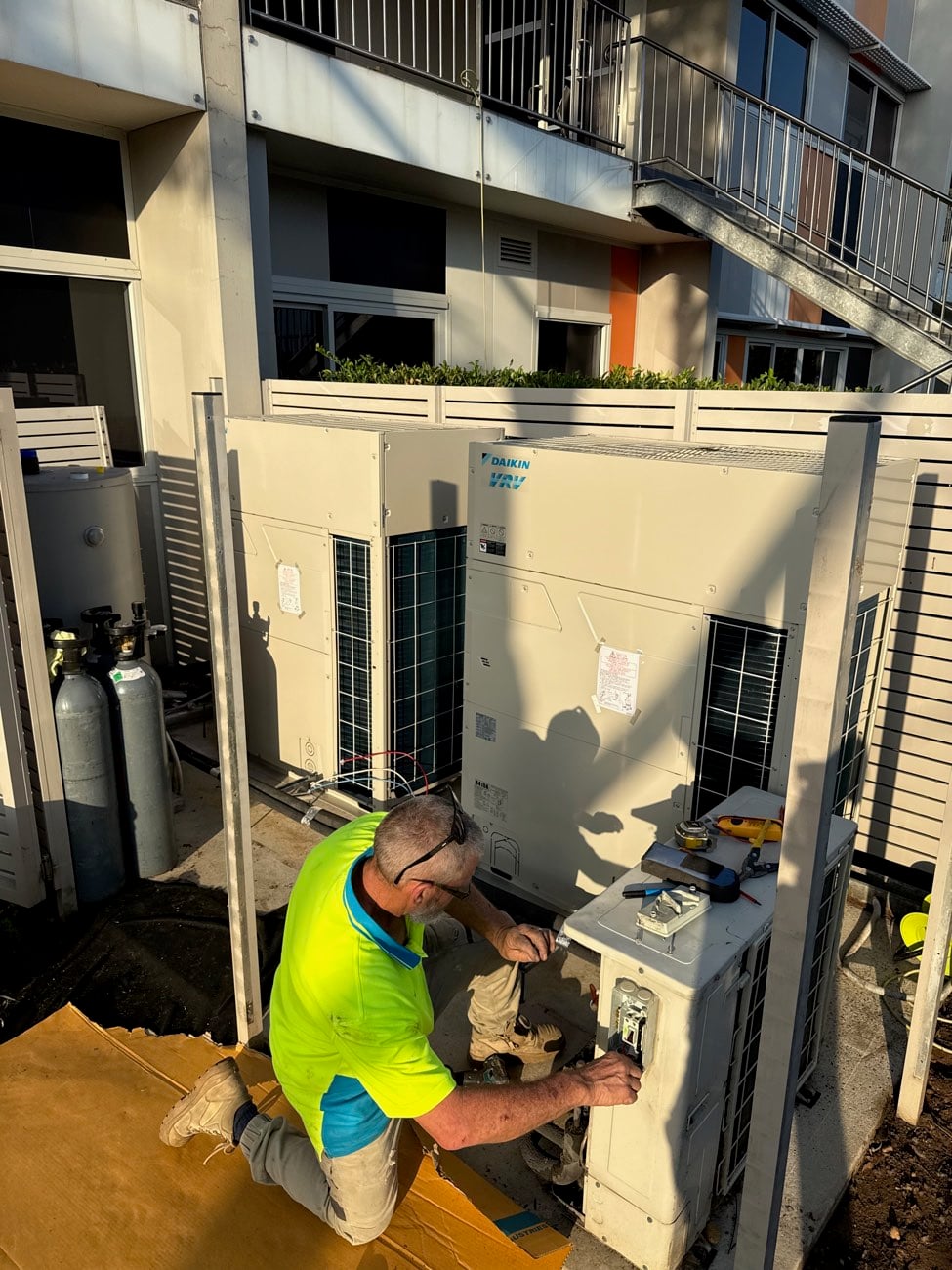 Ample Air technician working on Daikin VRV outdoor units in the afternoon sun